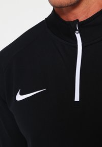 Pullover nero Nike con zip a quarti e logo bianco. Realizzato in tessuto testurizzato, presenta un colletto alto e una vestibilità atletica.