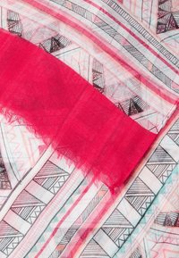 Tissu léger avec des motifs géométriques noirs et roses, partiellement recouvert par un tissu rose vif uni aux bords effilochés.
