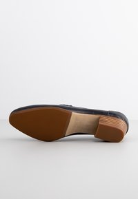 Chaussure de ville noire en cuir, retournée pour montrer sa semelle brune texturée, son talon en bois empilé et la taille 37 imprimée à l'intérieur.