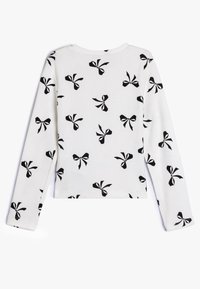 Maglietta a maniche lunghe in materiale a coste bianco con un motivo a fiocco nero ripetuto. Collo a giro con orlo dritto. Design semplice e testurizzato.