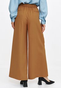 Szerokie brązowe spodnie z elastycznym paskiem w talii i dwiema tylnymi kieszeniami, zestawione z czarnymi szpilkami. Gładka faktura i prosty design.