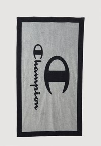 Harmaan ja mustan sävyinen kudottu peitto, jossa on sana "Championi" ja logo. Suorakulmainen muoto, teksturoitu kangas näkyvine ompeleineen ja reunuksineen.