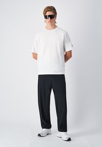 T-shirt bianco a maniche corte con scollo tondo, abbinato a pantaloni neri e scarpe da ginnastica bianche. Gli accessori includono occhiali da sole neri.