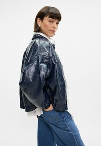 Tums zila mākslīgās ādas bombers jakas ar spīdīgu tekstūru, elastīgu jostasvietu, pārspīlētu siluetu un salokāmu apkakli.