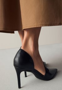 Czarny skórzany szpilka z ostrym noskiem i wycięciami po bokach, o eleganckim, błyszczącym wykończeniu i cienkim obcasie typu szpilka.