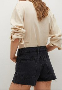 Camisa de manga larga de canalé en color crema con mangas enrolladas, combinada con pantalones cortos de mezclilla negros de tiro alto con dobladillos deshilachados y bolsillos traseros.