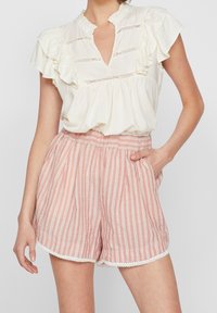 Blusa bianca con volant e scollo a V abbinata a pantaloni shorts a righe rosa chiaro, dotati di tasche e rifinitura in pizzo sull'orlo.