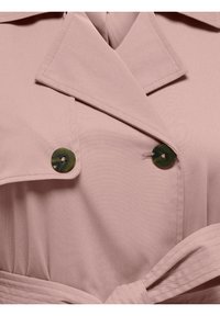 Trench-coat rose clair avec de gros boutons foncés, larges revers et ceinture cousue nouée à la taille.