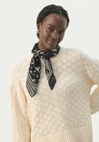 Elfenbensfarvet strikket sweater med et struktureret diamantmønster og ribbet kant, parret med et marineblåt tørklæde med blomster- og stribemønstre.