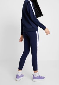 Námořnicky modrá atletická tepláková souprava s bílými postranními pruhy, legíny s úzkým střihem a dlouhý rukáv. Doplněná světle fialovými teniskami na platformě.