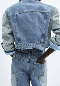 Veste en denim au design court, avec des panneaux de bleu clair et foncé contrastants, et des poignets de chemise rayés retroussés. Dispose de poches doubles.