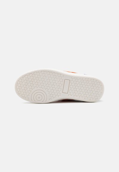 La suela del zapato presenta una base de goma blanca con un patrón hexagonal, un diseño circular en el talón y una superficie texturizada para mayor tracción.