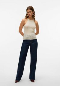 Top halter crema chiaro con scollatura a pettine e design a maglia testurizzata, abbinato a jeans a gamba larga blu scuro a vita alta.