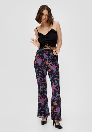 Zwart cropped top met verstelbare trekkoord, gecombineerd met uitlopende broek in een kleurrijk abstract patroon van paars, groen, rood en zwart.