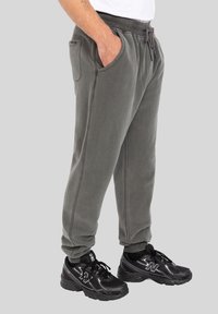 Szare dresowe spodnie z polaru z bocznymi kieszeniami, elastycznym paskiem w talii i sznurkiem do regulacji. W połączeniu z czarnymi butami sportowymi o teksturowanej powierzchni.