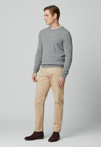 Grå ribbet sweater, beige chinos og brune ruskind ankelstøvler. Sweateren har en rund halsudskæring og tætsiddende cuffs.