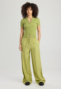 Vaaleanvihreä poimutettu lyhythihainen paita, jossa on nappisuljenta, yhdistetty löysiin yhteensopiviin housuihin, joissa on joustava vyötärö ja tekstuuri.