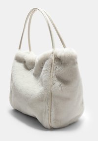 Borsa in pelliccia sintetica bianca con due manici lunghi, forma arrotondata e superficie texturizzata; presenta un aspetto morbido e soffice e una tonalità neutra.