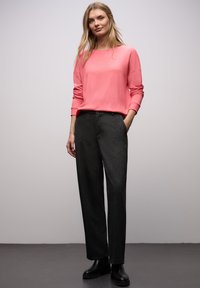 Jasnoróżowy sweter z długimi rękawami i prążkowanymi mankietami, zestawiony z ciemnoszarymi spodniami o szerokich nogawkach oraz czarnymi botkami za kostkę. Gładka faktura na całej powierzchni.