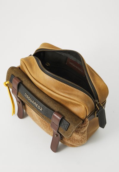 Geantă din piele maro și pânză, cu închidere cu fermoar, coasere la vedere și un fund asemănător cu suedeul. Dispune de o etichetă de marcă neagră și accesorii aurii.