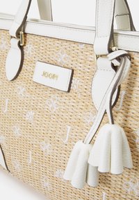 Sac en paille tressée avec des accents en cuir blanc, plaque logo en relief et franges décoratives. Présente un design structuré avec des détails en métal doré.