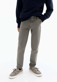 Pantaloni in denim grigio con vestibilità dritta, abbinati a un maglione blu navy e sneakers grigie con lacci e suola bianca.
