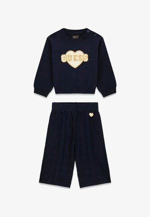 Granatowy sweter dziany z sercem i logo "GUESS", w połączeniu z dopasowanymi pikowanymi granatowymi spodniami z małym detalem w kształcie serca.