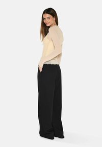 Beige långärmad topp med ribbat mönster och scalloperad nedkant, ihop med svarta vida byxor med sidofickor.