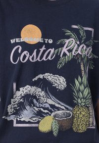 Navy blue T-shirt featuring a graphic design with palm trees, waves, a sun, and tropical fruits like a pineapple and coconut.