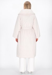 Geacă de fâș roz deschis, cu un guler mare, talie marcată cu curea și mâneci largi. Textură fină, cu un design minimalist și fără modele vizibile.
