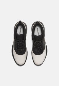 Černobílé sportovní boty s texturovaným svrškem, kulatou špičkou, šesti očky a vzorovanými tkaničkami. Logo je viditelné na stélce.