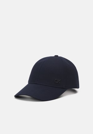 Granatowa czapka z daszkiem z wygiętym daszkiem i małym czarnym logo "CK" z przodu, przedstawiona na jednolitym białym tle.