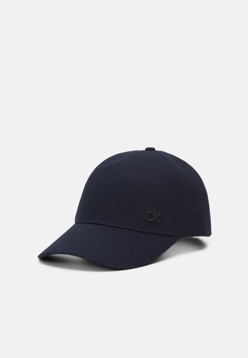 Casquette de baseball bleu marine avec visière courbée et petit logo noir « "CK" » à l'avant, présentée sur fond blanc uni.