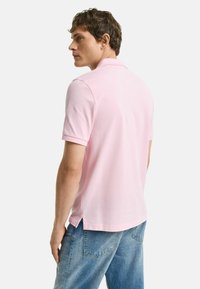 Polo shirt rosa in cotone, con colletto classico, maniche corte e spacchetti laterali, abbinato a jeans in denim blu chiaro.
