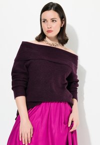 Maglione a spalle scoperte di un viola scuro a coste con maniche lunghe; indossato con una gonna rosa lucida, che mette in mostra un contrasto di tessuti texture.