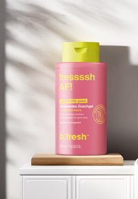 Roze douchegel fles met een gele dop. Bevat vetgedrukte tekst in het geel. Inhoud: 473 ml, vegan-vriendelijk recept. Houten basis, neutrale achtergrond.