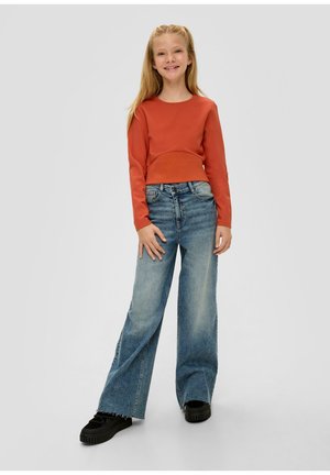 Rostfarbendes Langarmoberteil mit gerippter Textur, kombiniert mit weit geschnittenen hellblauen Jeans und schwarzen Plateausneakern mit strukturierten Sohlen.