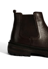 Bruine leren laars met elastische zijpanelen en een gestructureerde afwerking. Dikke rubberen zool met een uitgesproken profiel voor grip.