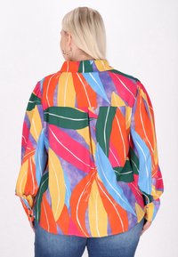 Cămașă colorată cu nasturi, având un model abstract îndrăzneț de frunze în nuanțe de roșu, verde, galben, albastru și violet pe un fundal deschis.