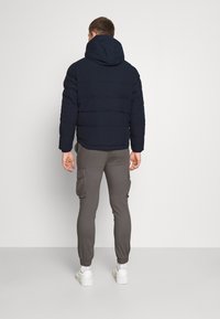 Granatowa kurtka puchowa z kapturem, z pikowanymi sekcjami i elastycznymi mankietami, noszona na szarych spodniach dresowych typu cargo z bocznymi kieszeniami i elastycznymi zakończeniami nogawek.