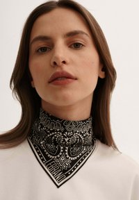 Czarnobiały szalik w wzór paisley, o trójkątnym kształcie i kontrastowym wykończeniu, noszony na szyi.