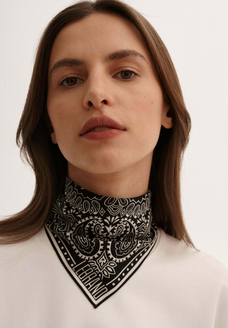 Czarnobiały szalik w wzór paisley, o trójkątnym kształcie i kontrastowym wykończeniu, noszony na szyi.