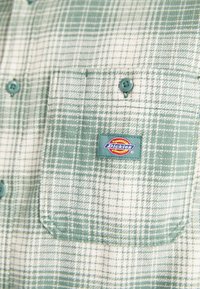 Žaliai ir baltai daugiaplanuota ilgomis rankovėmis marškinėliai, su krūtinės kišene, ant kurios yra "Dickies" logotipo etikete ir mėlynais mygtukais. Medvilnė, tekstūruotas dizainas.