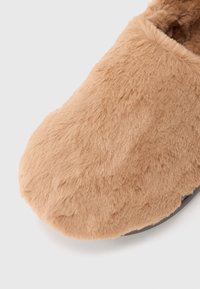 Myk, lys brun faux fur innesko med avrundet tå og mørk såle, vist fra topp-front vinkel på hvit bakgrunn.
