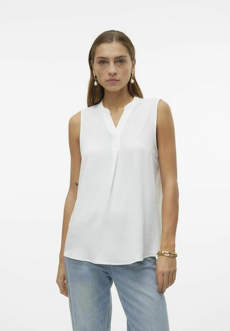 Haut sans manches blanc avec un décolleté en V et une texture subtile, associé à un jean en denim bleu clair. Le tissu semble doux et léger.