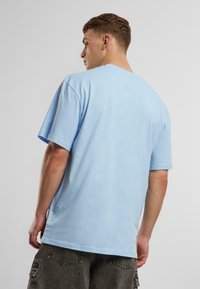 T-shirt en coton bleu clair avec une coupe décontractée, des manches courtes et un col rond, vue de dos. Aucun motif ou accent notable visible.