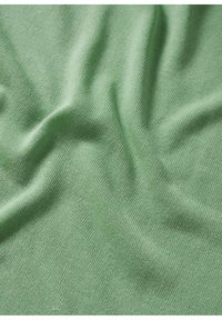 Tissu en coton vert avec une texture douce, présentant un tissage lisse légèrement extensible et des plis subtils.