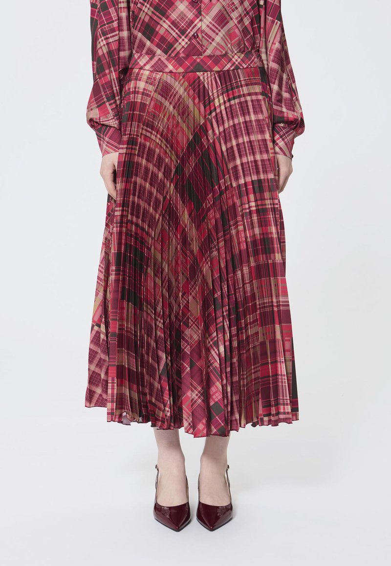 Gonna lunga plissettata in rosso con motivo a scacchi in diverse tonalità di rosa, verde e nero; abbinata a décolleté borgogna a punta.