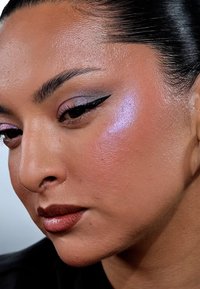Primo piano di un volto con una pelle liscia e radiosa. Presenta ombretto nei toni del viola, eyeliner ben definito e un colore di labbra morbido e lucido.