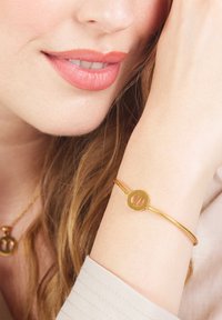 Gouden armband met een ronde bedel met uitgesneden ontwerp, een gladde metallic afwerking, gedragen om een pols, tegen een neutrale achtergrond.